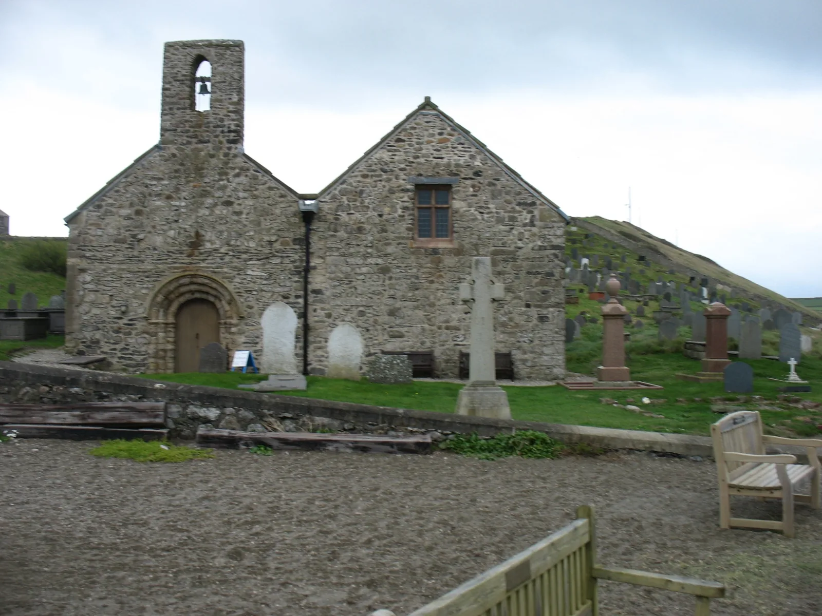 The west front of St Hywyn’s Church, Aberdaron, its Romanesque arched door and bellcote above the headstones