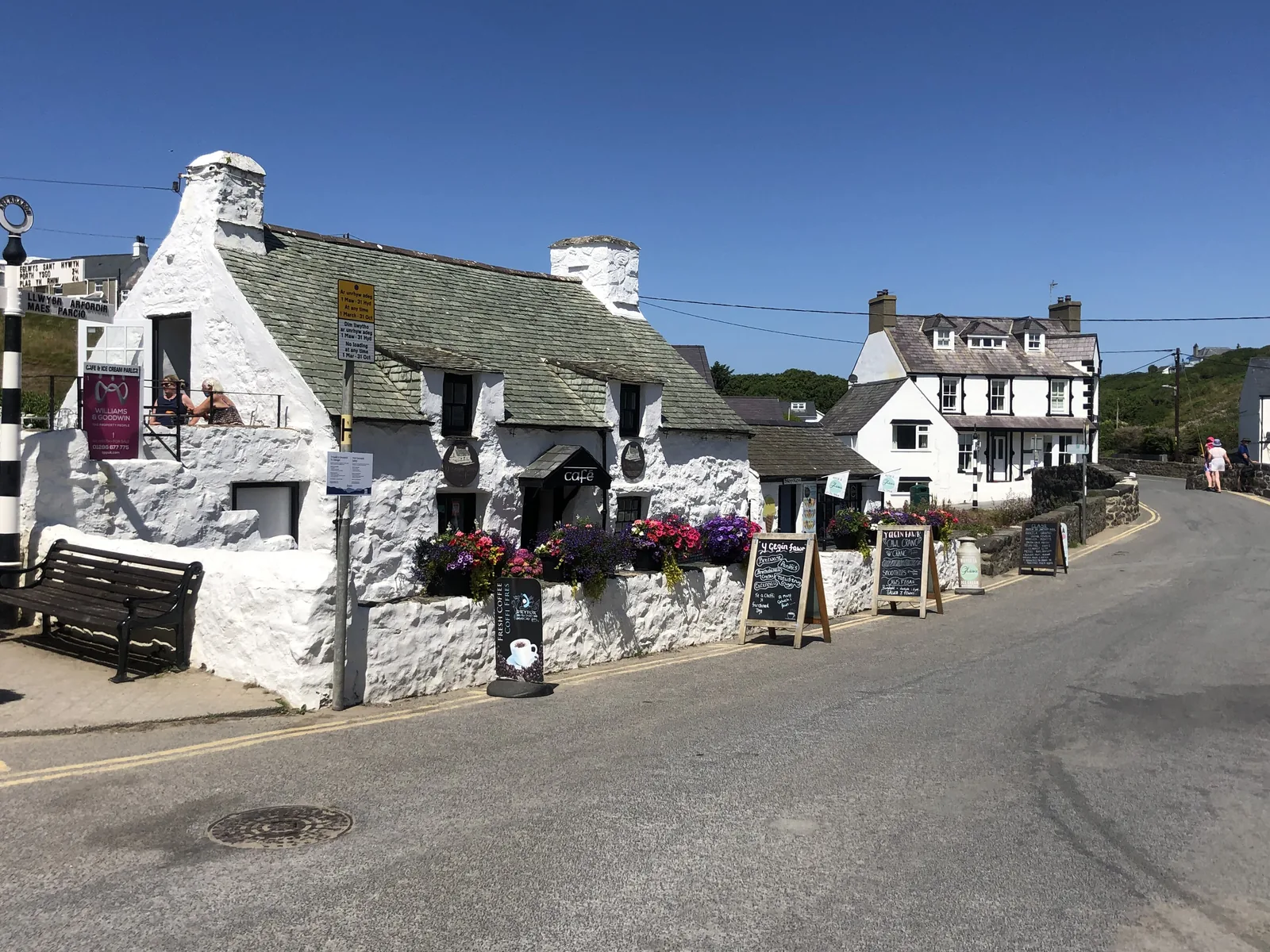 Y Gegin Fawr, a low whitewashed building with hanging baskets, standing on the corner in the centre of Aberdaron