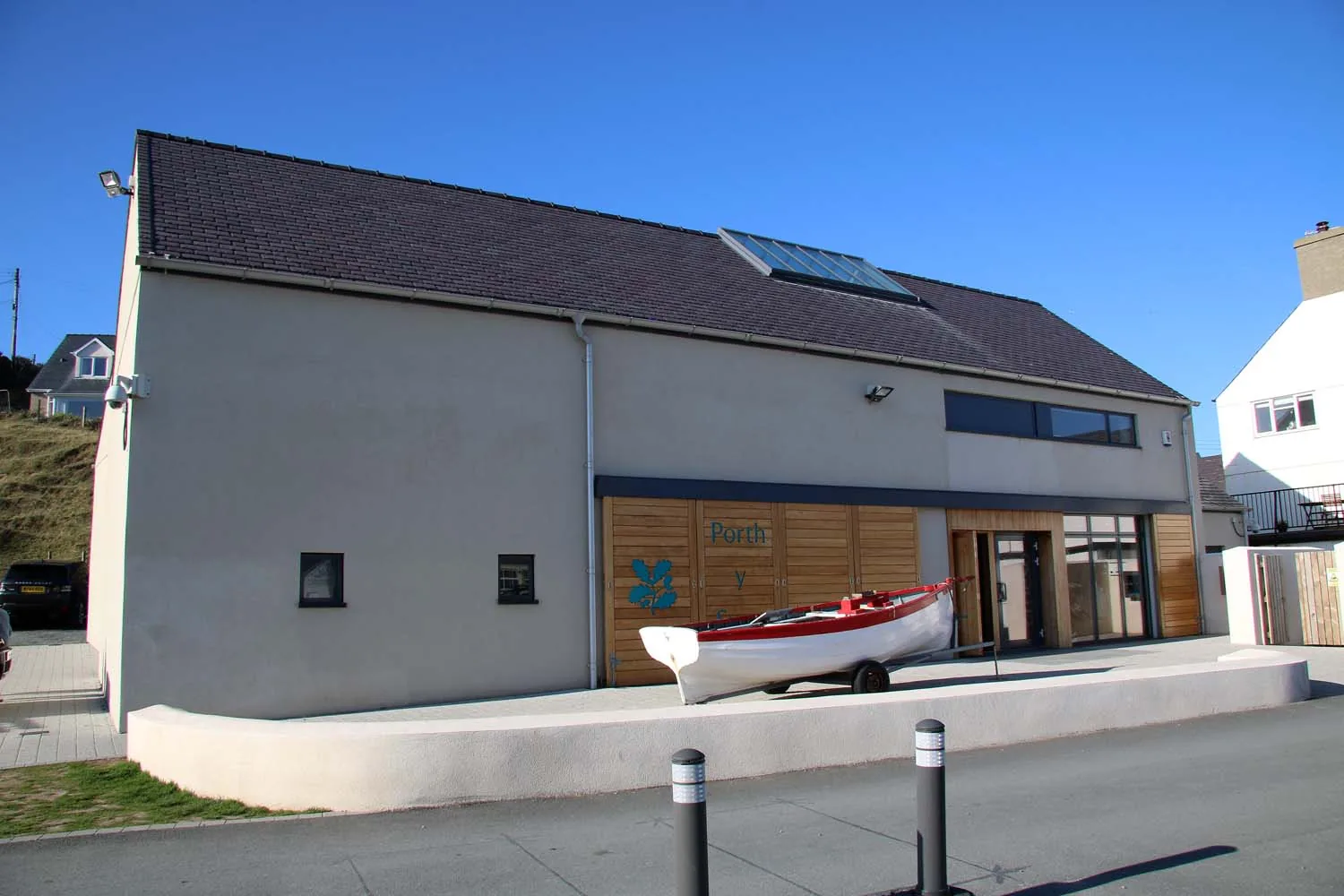 Porth y Swnt, a low white National Trust building in the centre of Aberdaron with a wooden boat outside it