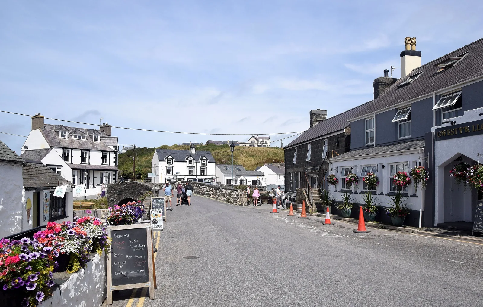 The main street through Aberdaron, whitewashed and stone frontages with flower baskets and people walking in the middle distance