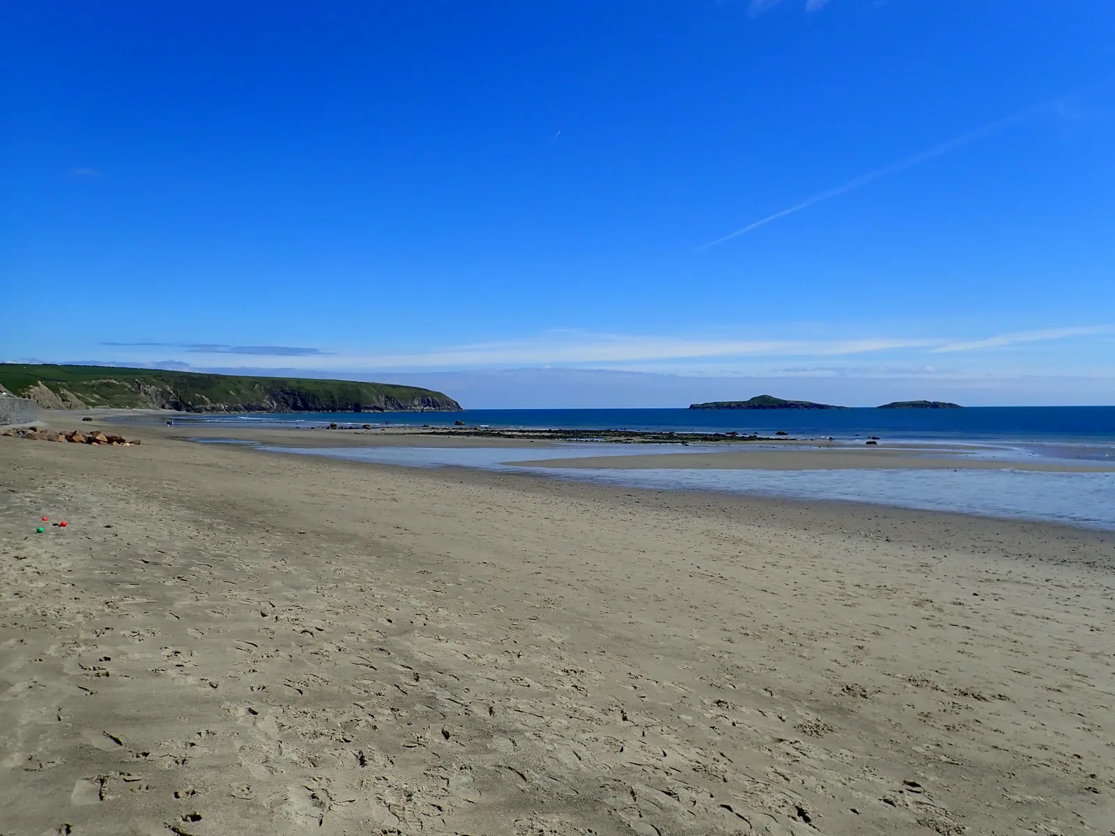 Aberdaron beach at low tide, wet sand running out to a flat sea with the islands beyond