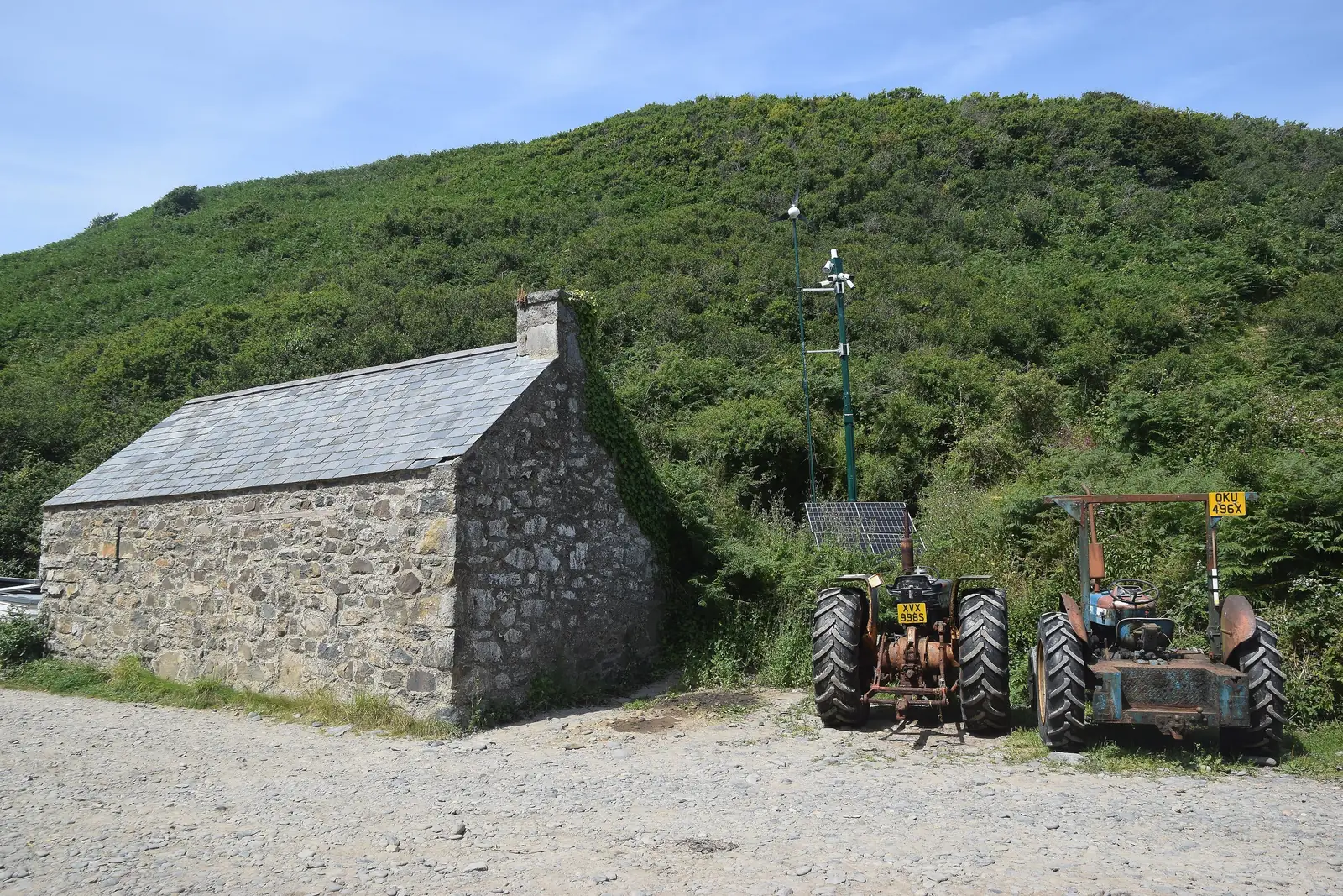 A stone outbuilding and parked tractors at the top of the track down to Porth Meudwy, bracken slopes rising behind