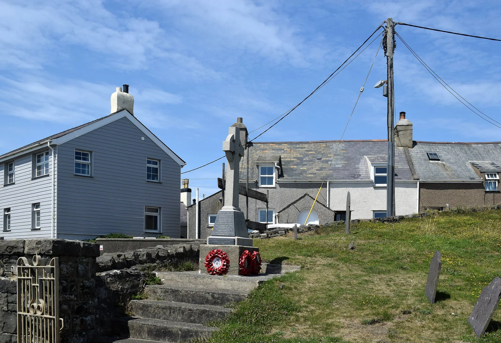 Aberdaron’s stone war memorial cross with wreaths at its foot, houses and telegraph poles behind