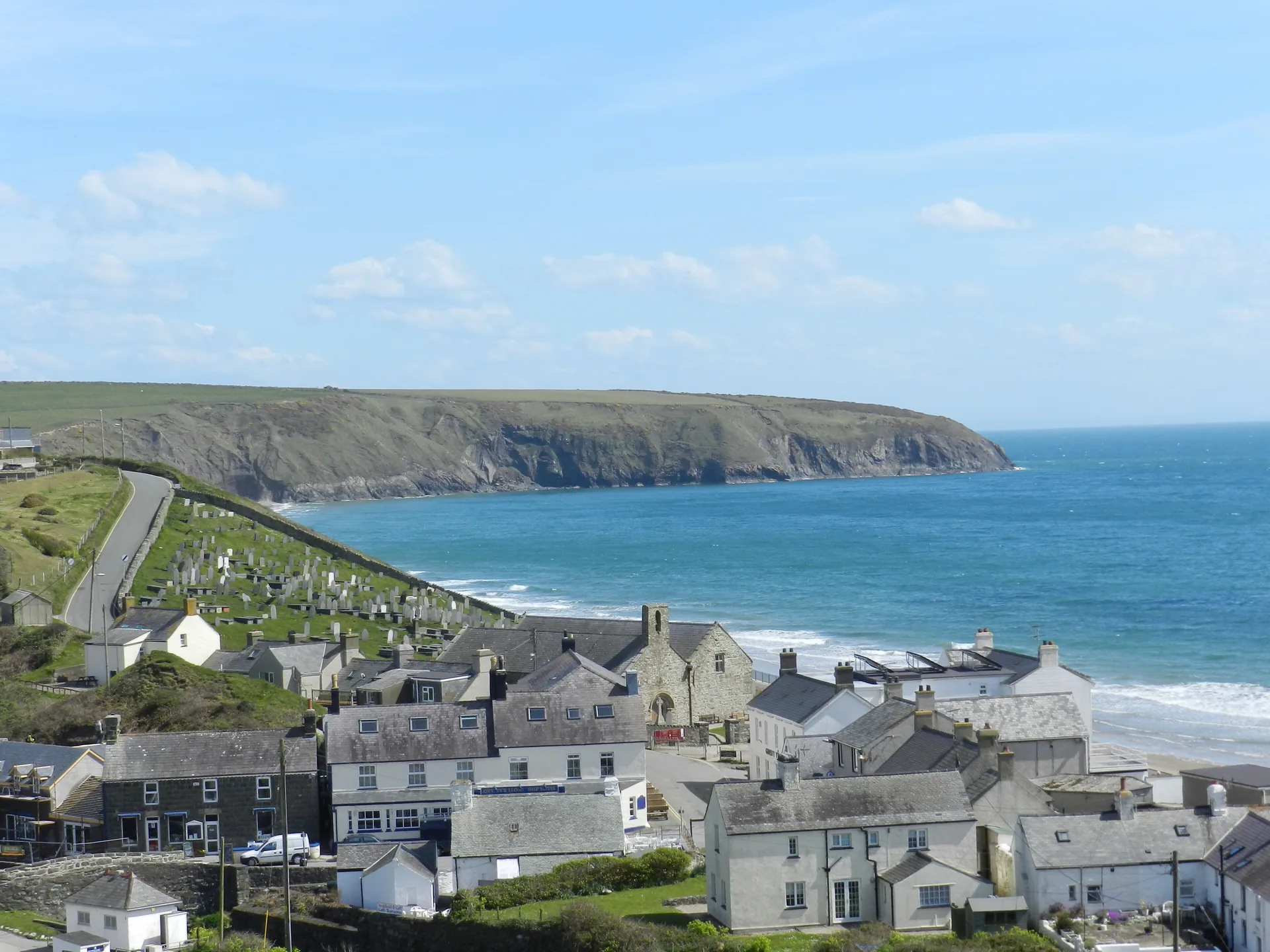 Aberdaron&rsquo;s white houses stacked above the sand, the bay opening south past a green headland to the sea