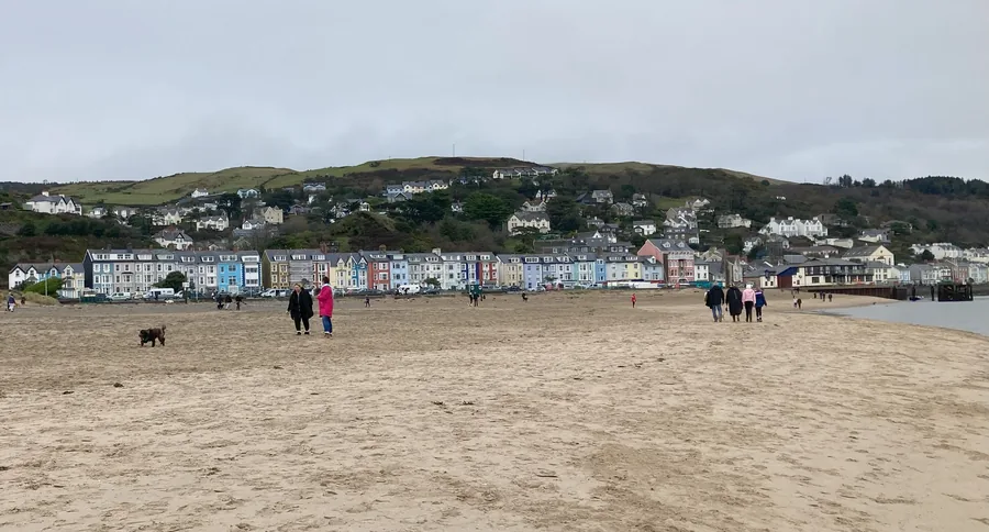 Aberdyfi's painted seafront terraces seen from the sand, walkers on the beach and the jetty at the far end