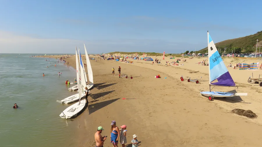 Aberdyfi's painted seafront terraces seen from the sand, walkers on the beach and the jetty at the far end, Gwynedd.