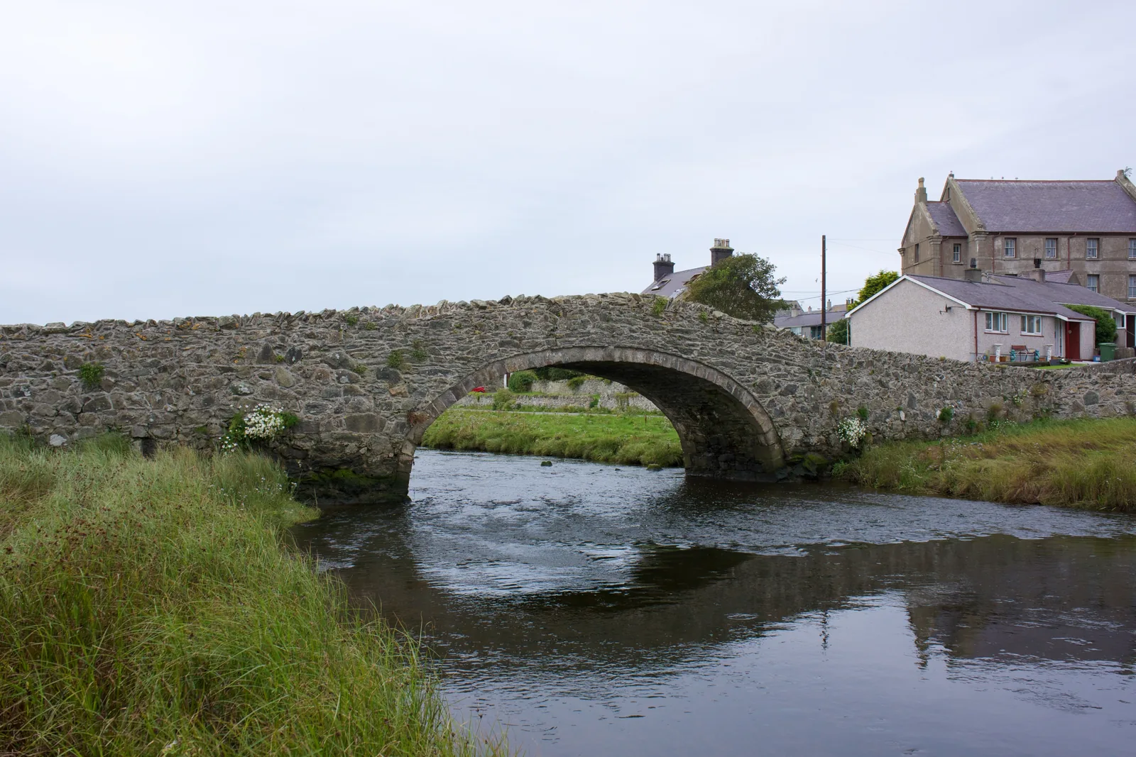 The single stone arch of Pont Aberffraw crossing the Afon Ffraw, reflected in the water below