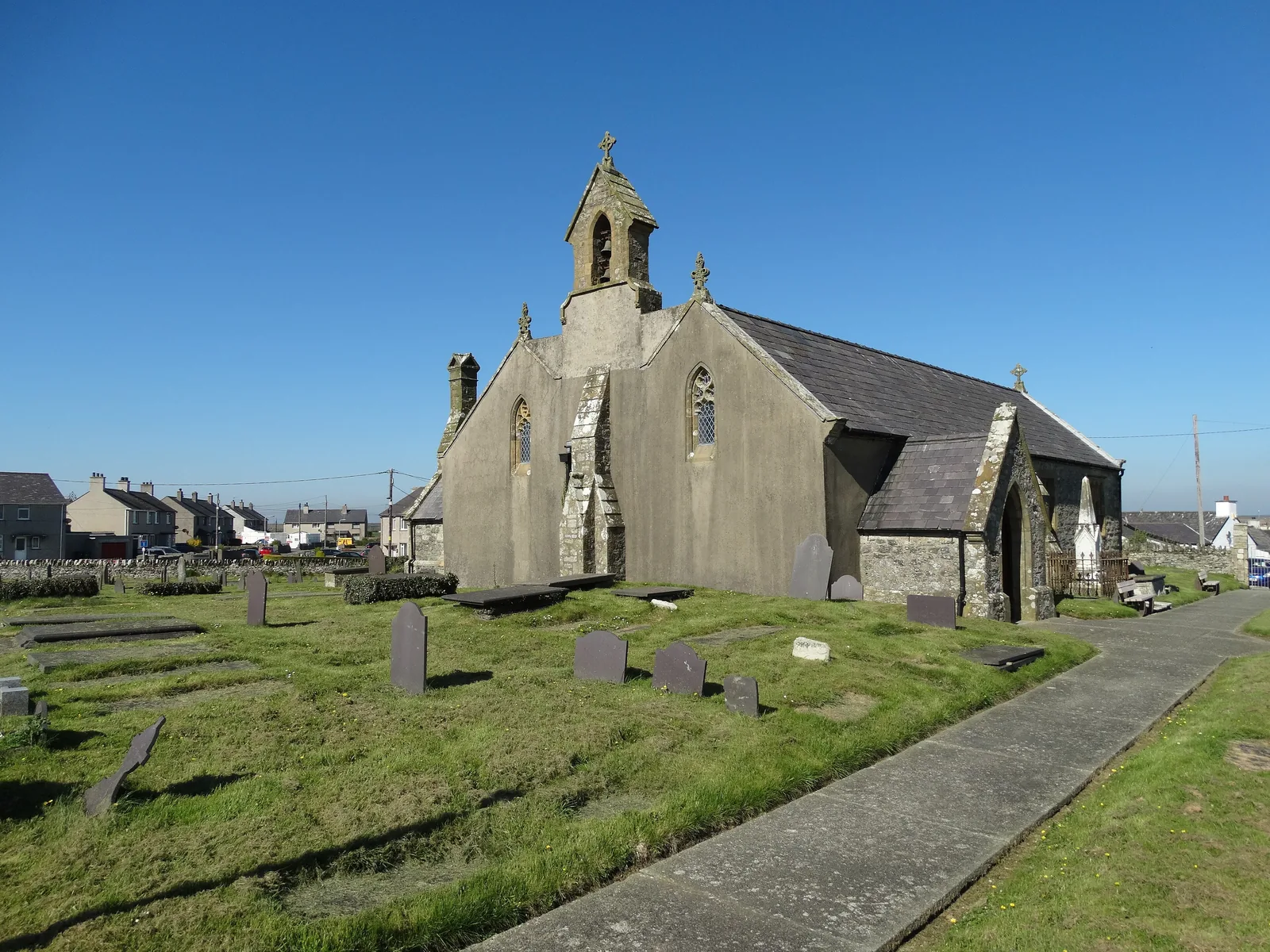 St Beuno's Church, Aberffraw, its bellcote and stone walls above the graveyard, with the path leading in from the gate