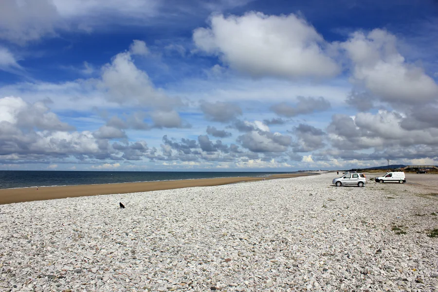 The white shingle bank at Pensarn beach under a wide cloudy sky, sand and sea beyond.