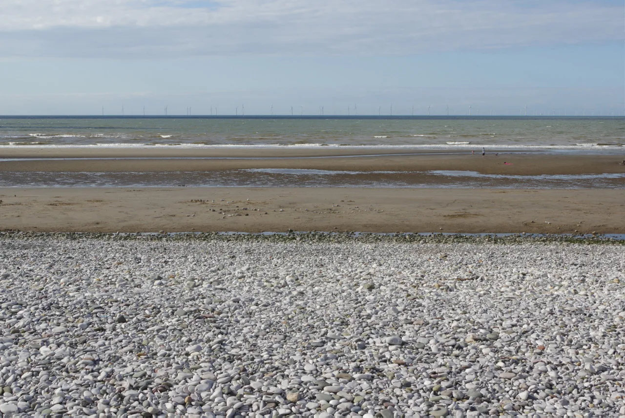 Pensarn beach at low tide, the shingle ridge in the foreground giving way to wet sand and shallow pools
