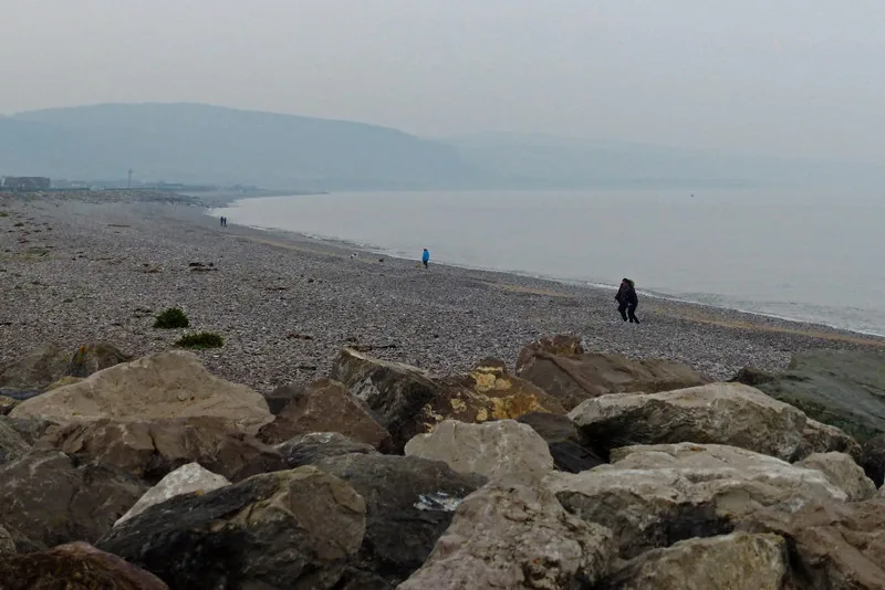 Rock armour along the shore at Pensarn, the shingle beach and the wooded coastal hills running away west