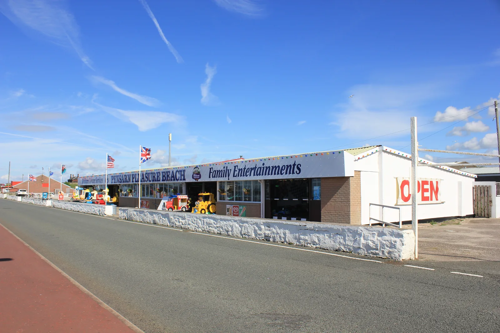 A low white amusement building on the front at Pensarn, flags along its roofline and the promenade running past it under a blue sky