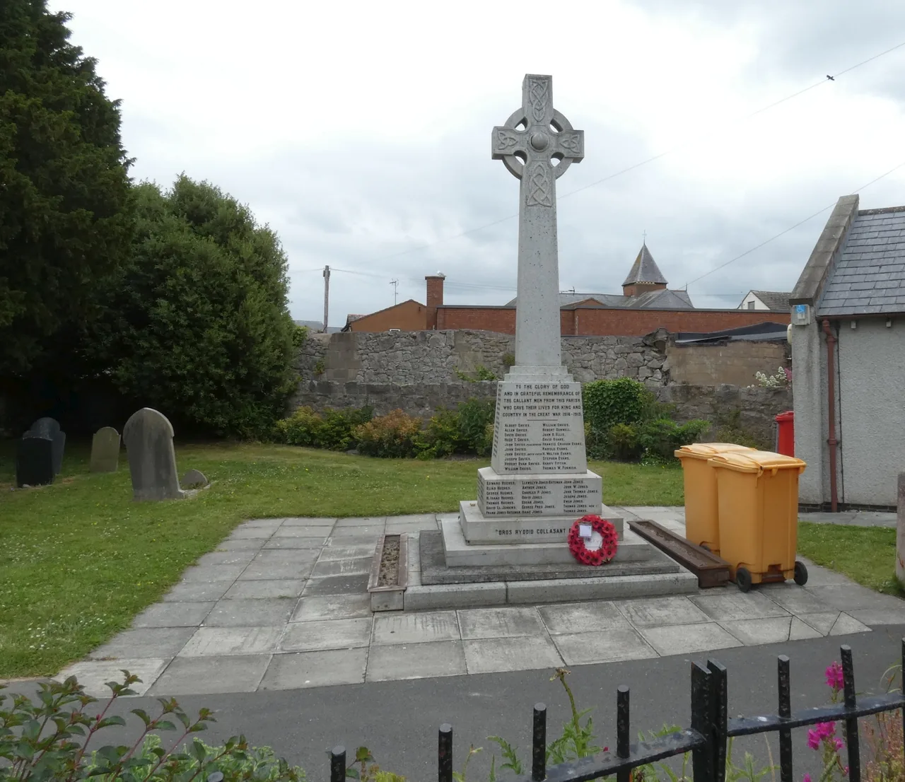 Abergele&rsquo;s stone Celtic-cross war memorial on its plinth, hedge and churchyard wall behind