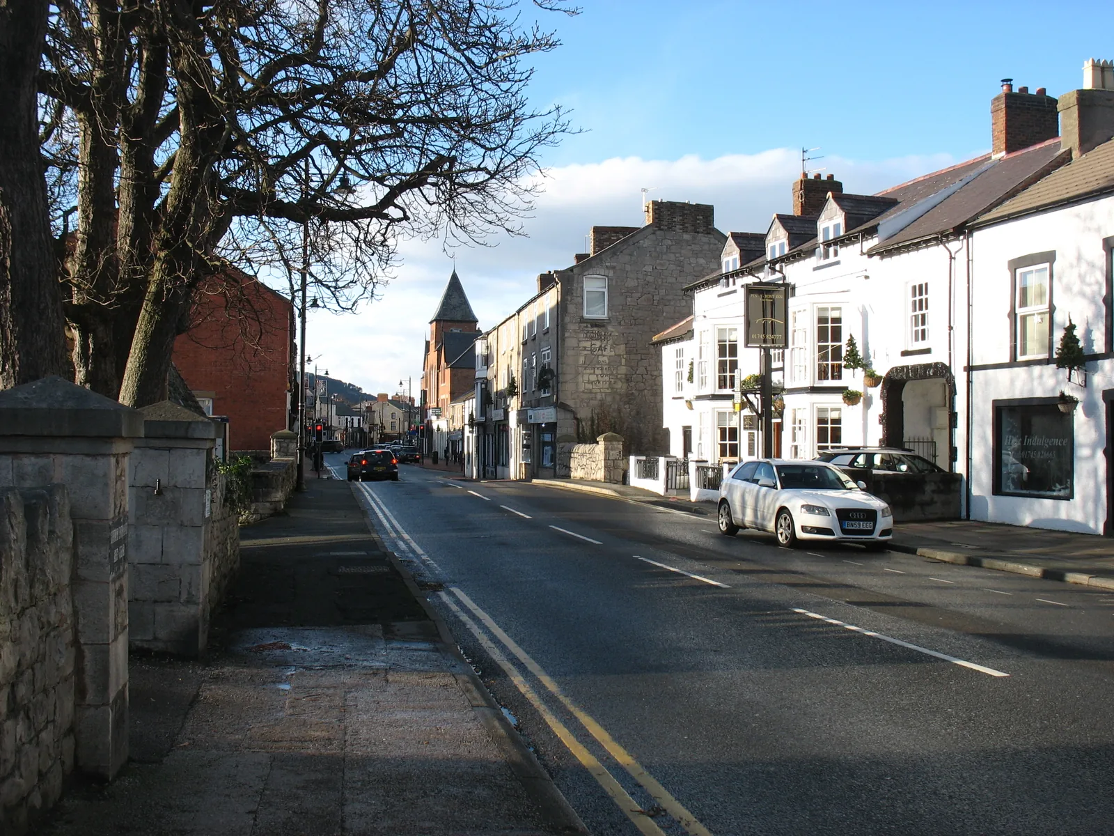 Abergele High Street looking west, parked cars and shopfronts along both sides