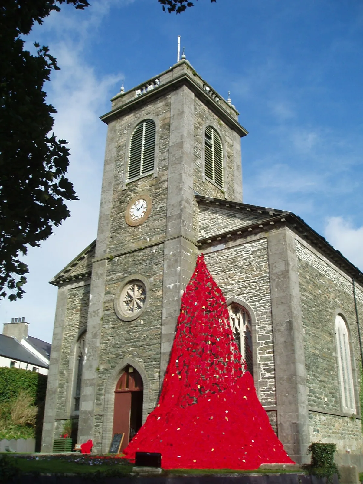 A cascade of knitted red poppies made by the community pouring down the wall of St Eleth's Church, Amlwch