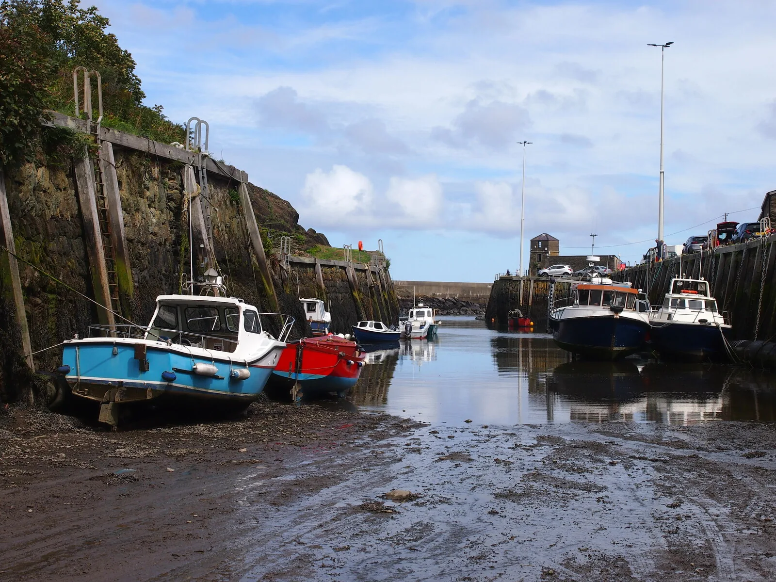 The inner harbour at Porth Amlwch at low tide, fishing boats resting against timber staging, the Watch House tower at the head of the inlet