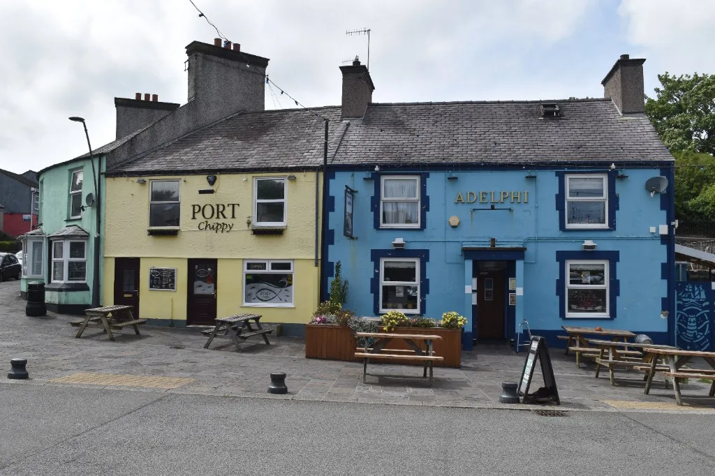 Painted buildings and picnic benches around the small square at Amlwch Port, planters in flower along the pavement
