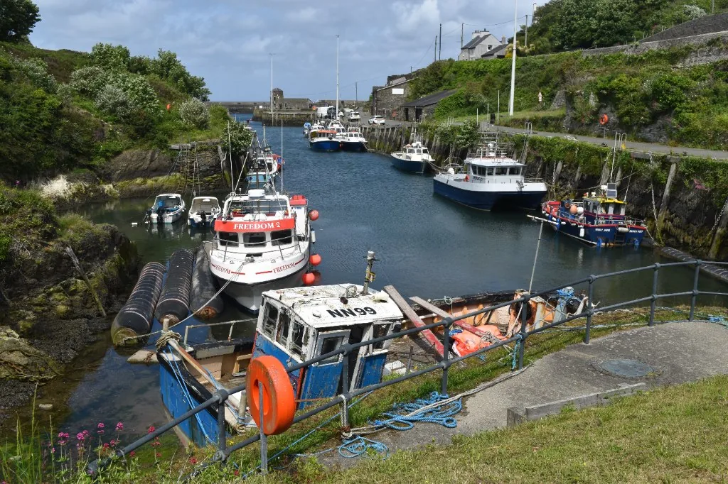 Fishing and pleasure boats moored along both walls of Amlwch harbour, coiled blue rope and an orange lifebuoy on the quayside in the foreground
