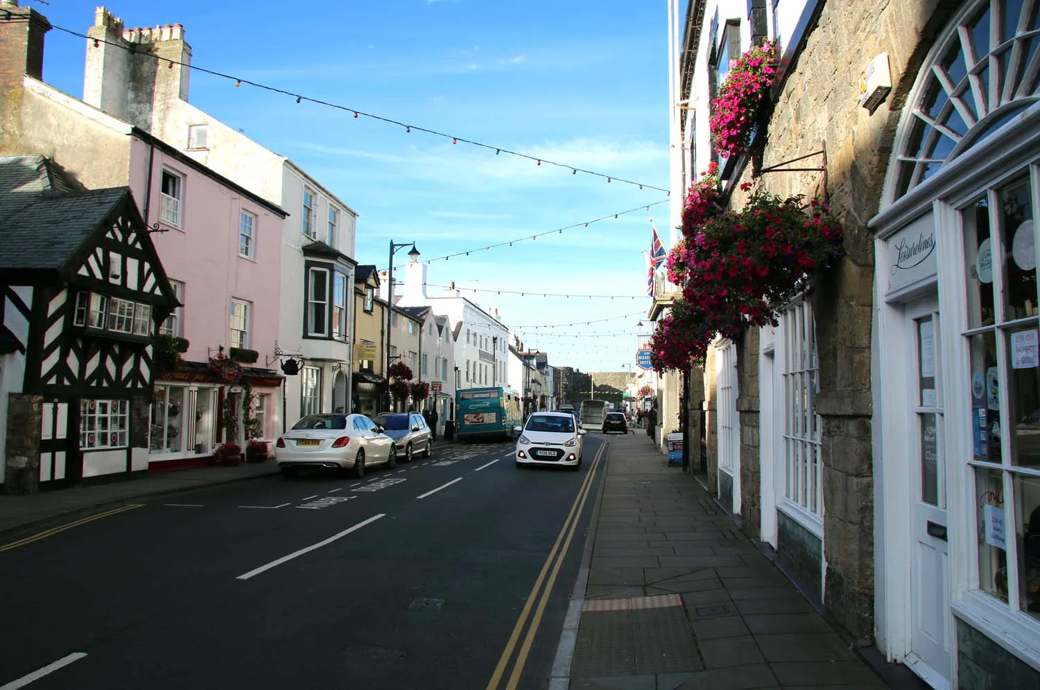 Castle Street, Beaumaris: painted Georgian shopfronts and the timber-framed Tudor Rose beneath hanging flower baskets.