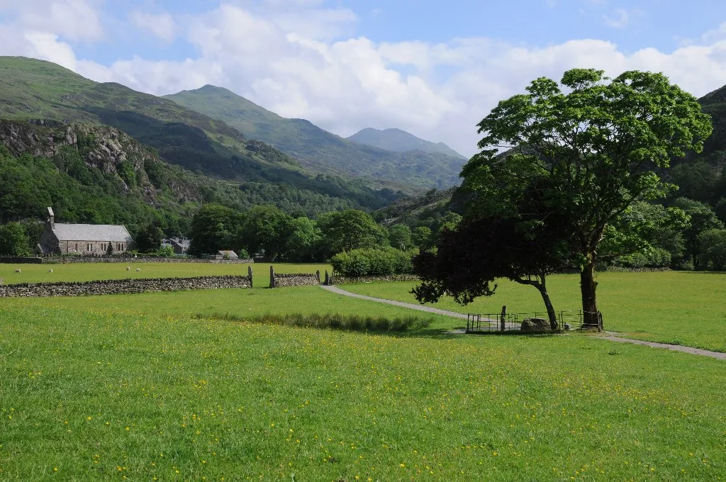St Mary's Church and Gelert's Grave in their meadow beside the Afon Glaslyn, the mountains of Eryri behind Beddgelert