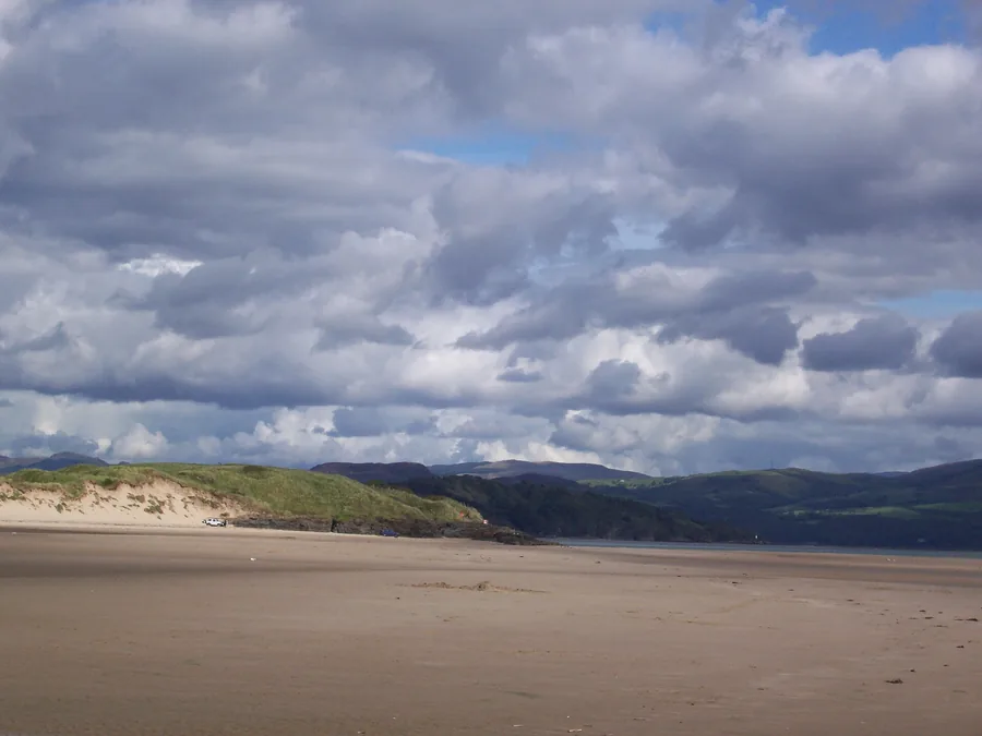 Black Rock Sands seen from the dunes, with vehicles parked on the wide, flat sand and hills across the bay.