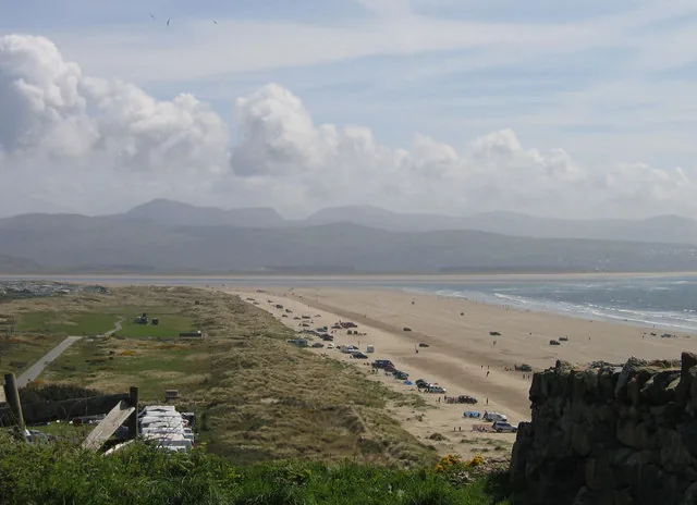 Black Rock Sands seen from the dunes, with vehicles parked on the wide, flat sand and hills across the bay.