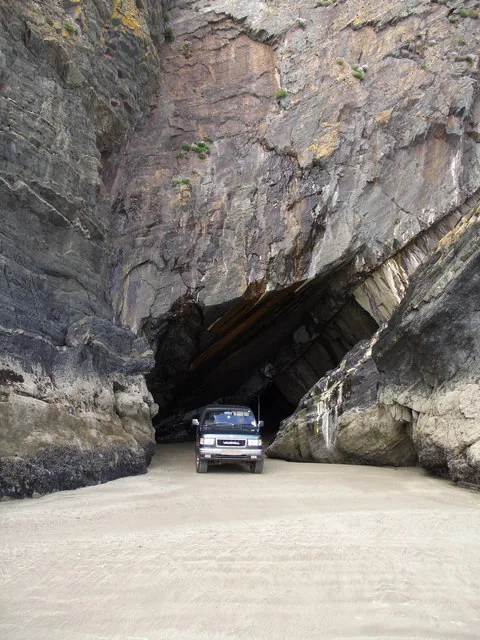 A car driving through a sea cave in the rock headland at Black Rock Sands.