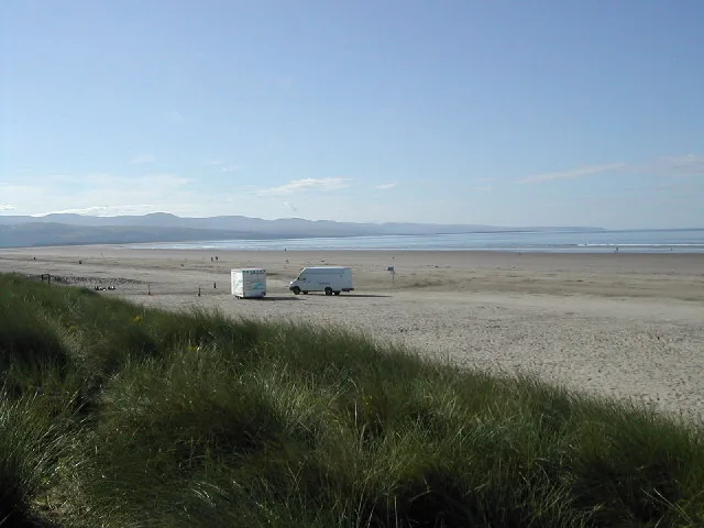 Marram grass in the foreground with a van parked on the open sand at Black Rock Sands, sea in the distance.