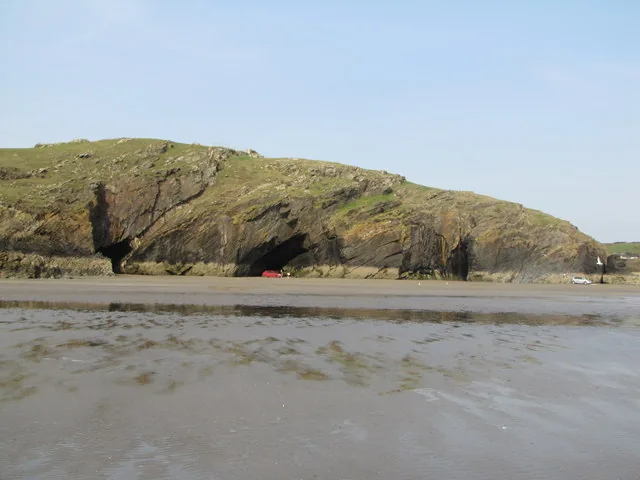 Sea caves cut into the rocky headland at Black Rock Sands, with a car parked near one entrance at low tide.