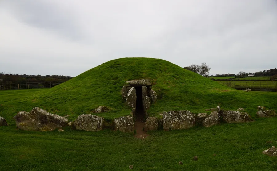 The grass-covered mound of Bryn Celli Ddu with its stone passage entrance on the east side, ringed by kerb stones in open farmland near Llanddaniel Fab, Anglesey.