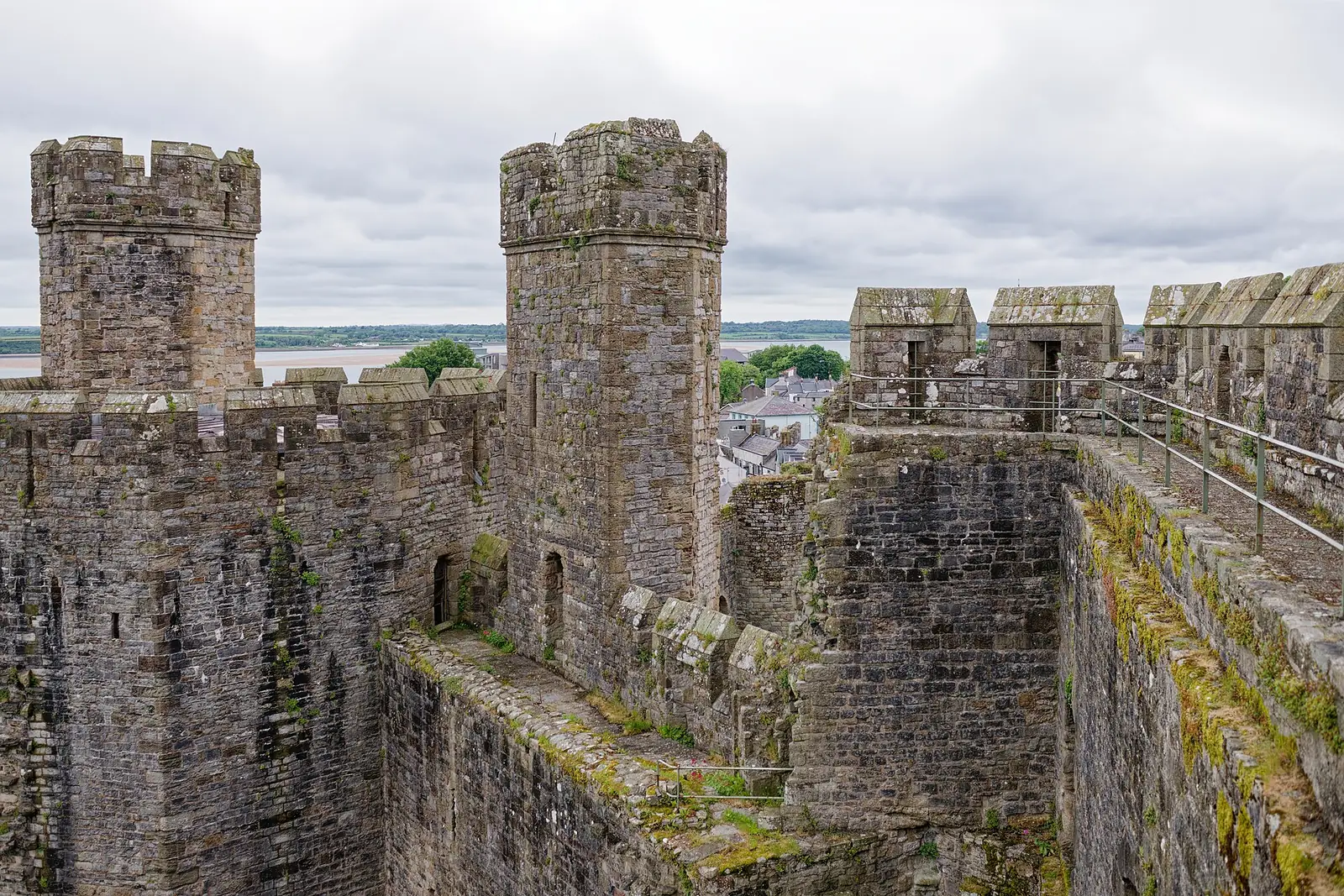 The battlements at Caernarfon Castle's Queen's Gate, twin towers and stone sentry boxes along the wall-walk above the town rooftops.