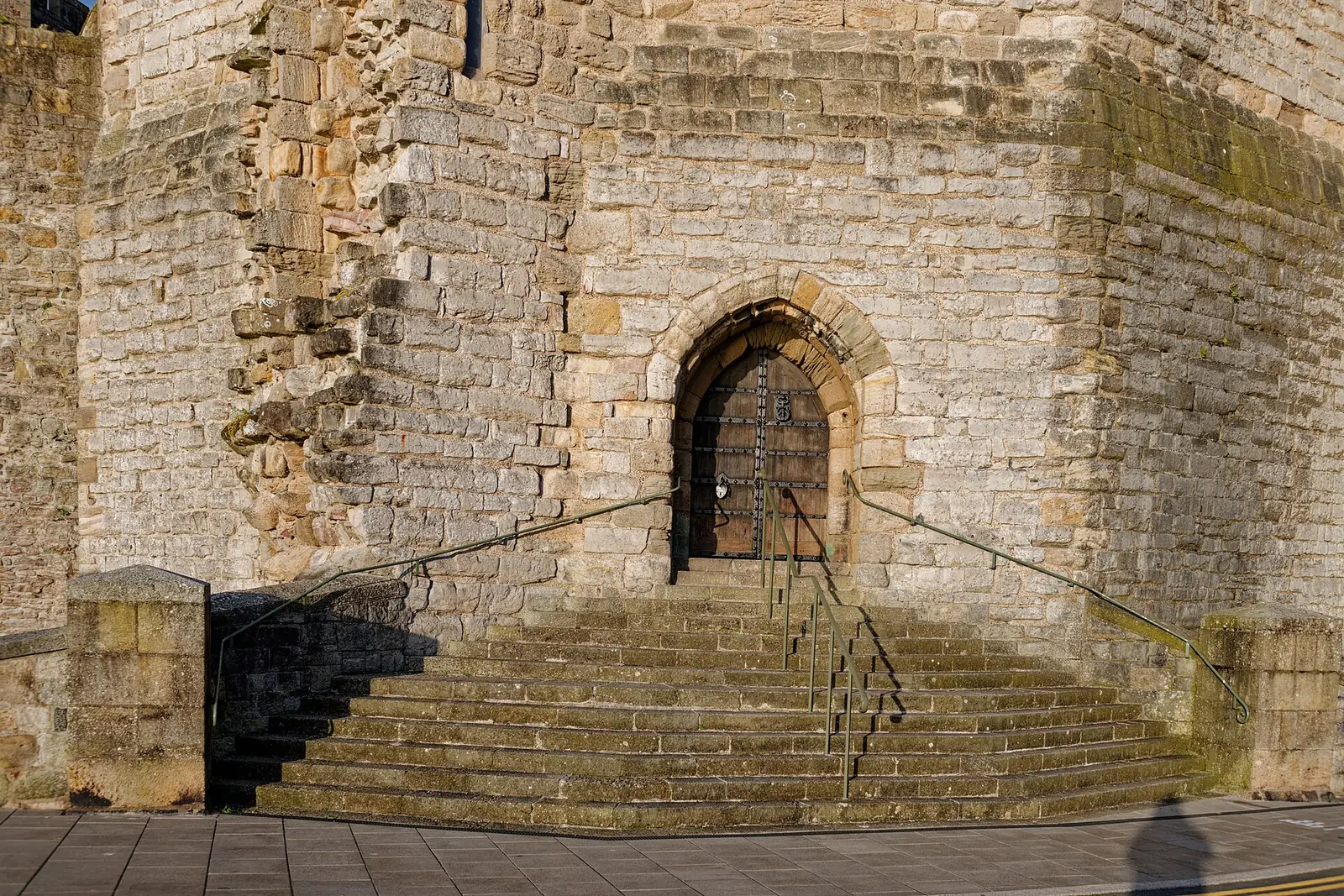 Close view of the Eagle Tower's stone staircase and arched wooden door at Caernarfon Castle, banded limestone and sandstone walls in warm evening light.