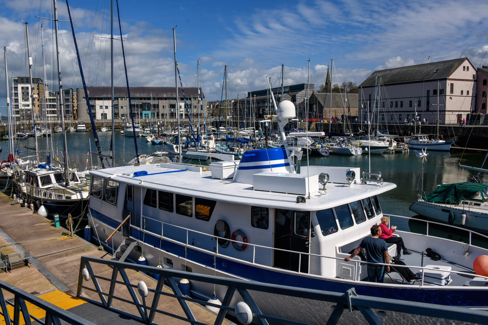 A boat alongside the pontoon at Victoria Dock marina, Caernarfon, with the quayside buildings behind