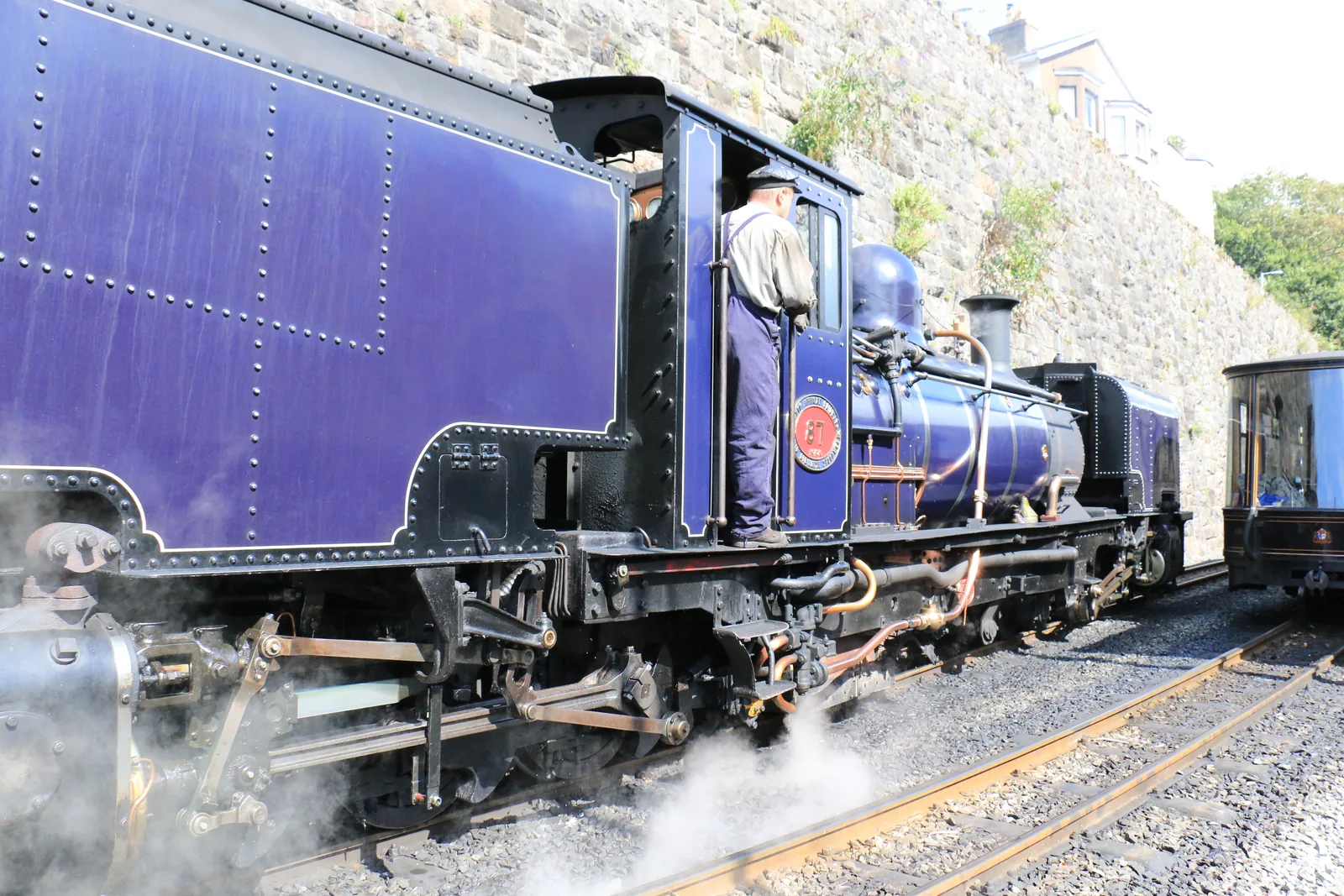 A blue Garratt locomotive in steam beside the retaining wall at Caernarfon