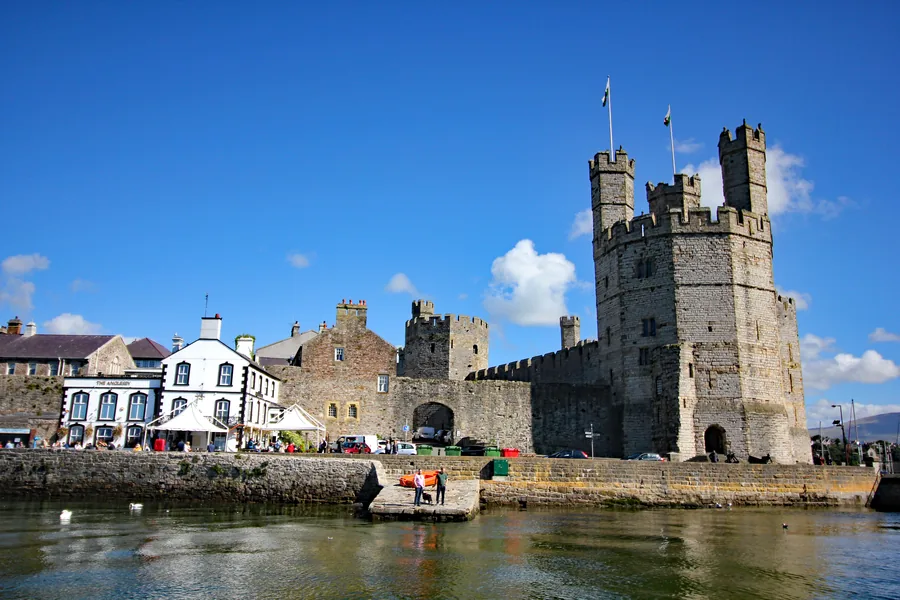 Caernarfon seen across the foreshore at low tide, the full run of its medieval town wall leading to the castle at the far end, Gwynedd.