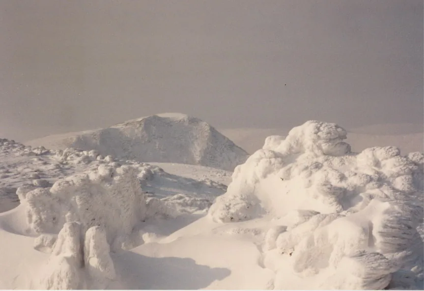 Full snow cover at the summit cairn of Carnedd Llewelyn, looking toward Yr Elen