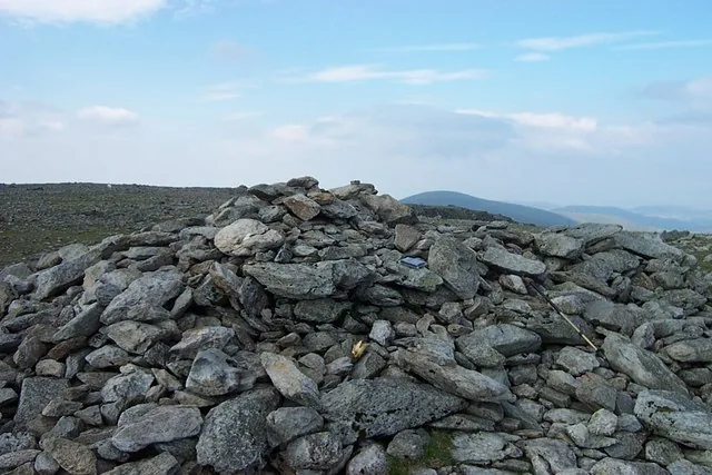The main summit cairn of Carnedd Llewelyn, on the broad stony plateau, with a hazy skyline beyond