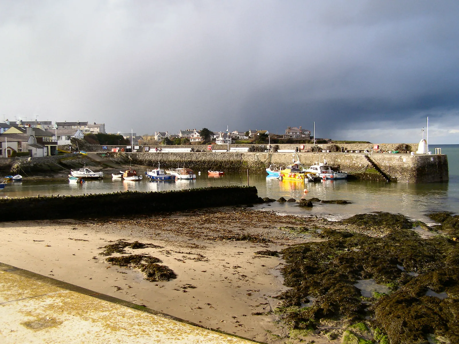 Boats moored inside the stone breakwater at Cemaes Harbour under a dark sky