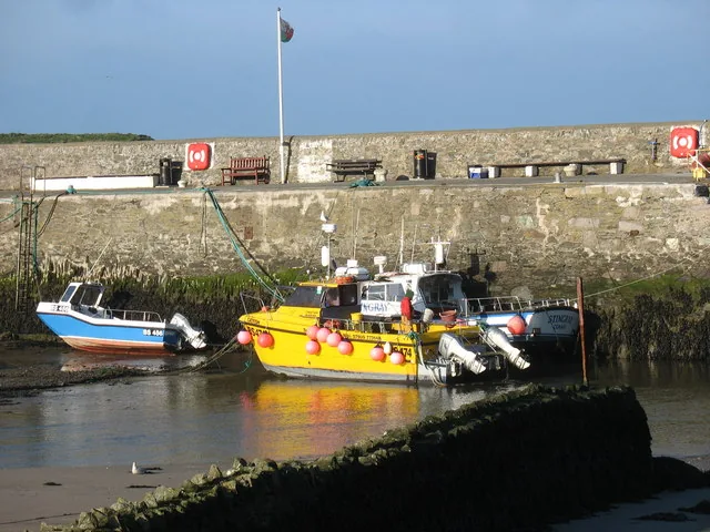 Small fishing boats with buoys and pot markers alongside the harbour wall at Cemaes