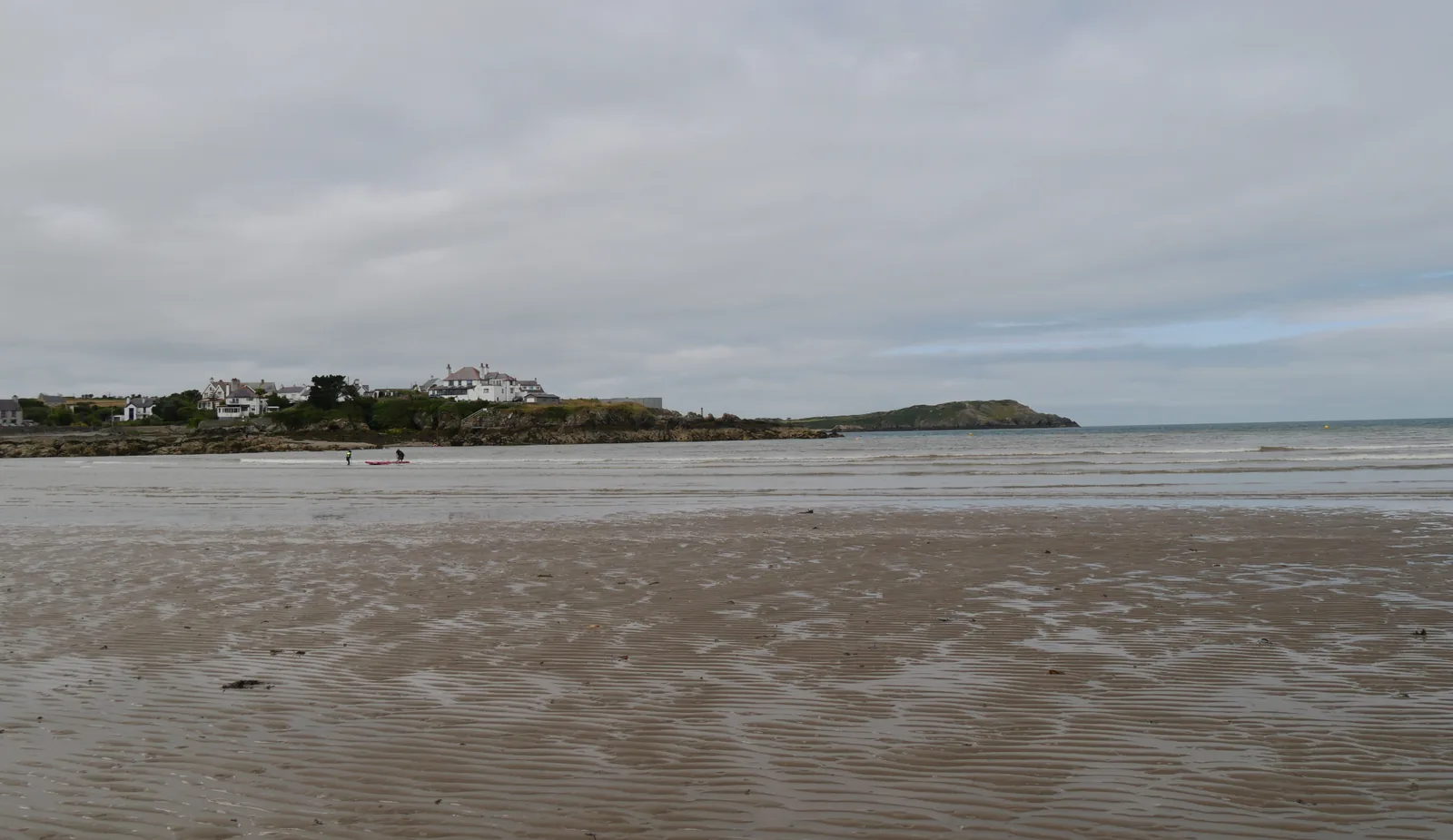Cemaes Bay seen along Traeth Mawr at low tide, with the houses and the eastern headland beyond