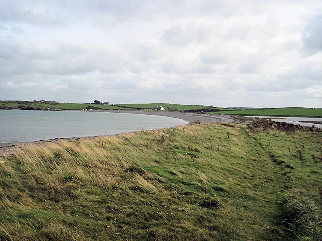 The shingle spit of Esgair Cemlyn curving along Cemlyn Bay, windblown grass in the foreground and farmland beyond.
