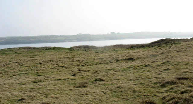 The grassy Trwyn Cemlyn headland looking across a misty Cemlyn Bay.
