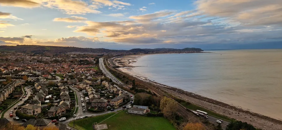 Colwyn Bay seen from Penmaenhead at dusk, the beach curving away west with the town spread up the slope behind it.