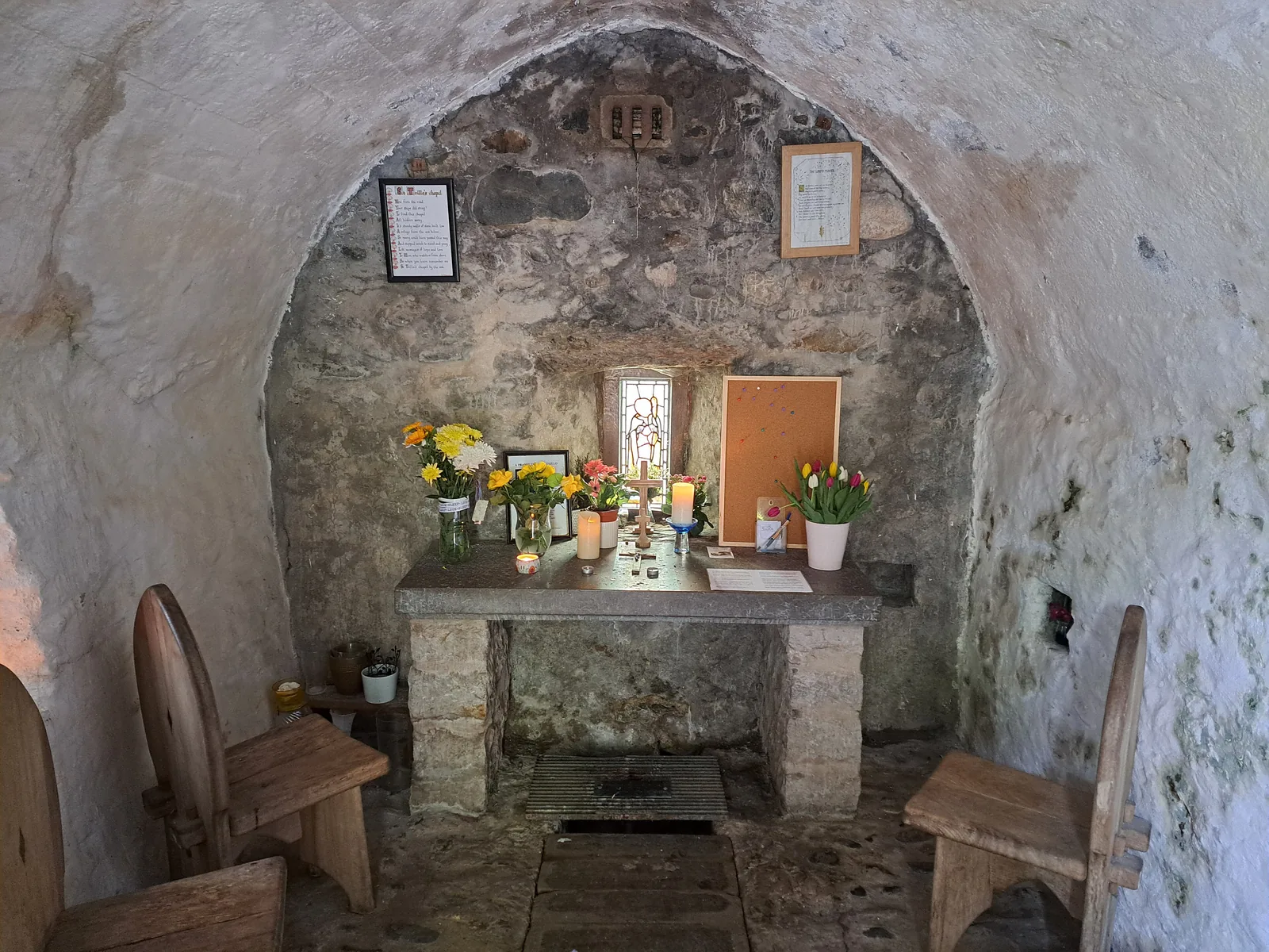 Inside St Trillo's Chapel at Rhos-on-Sea, a barrel-vaulted stone room with flowers on the altar built over the spring