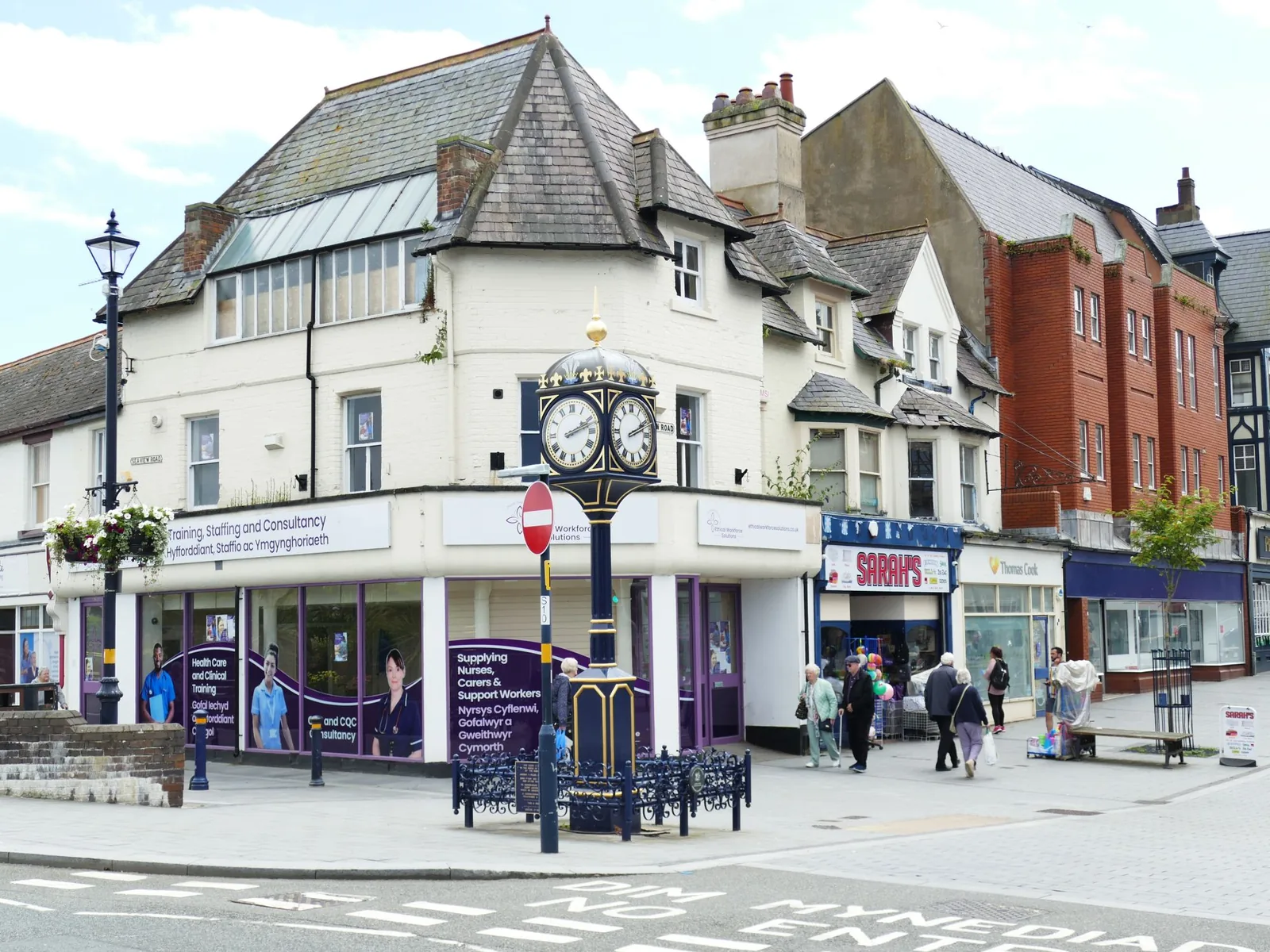 The town clock on Station Road, Colwyn Bay, with shoppers and shopfronts around it