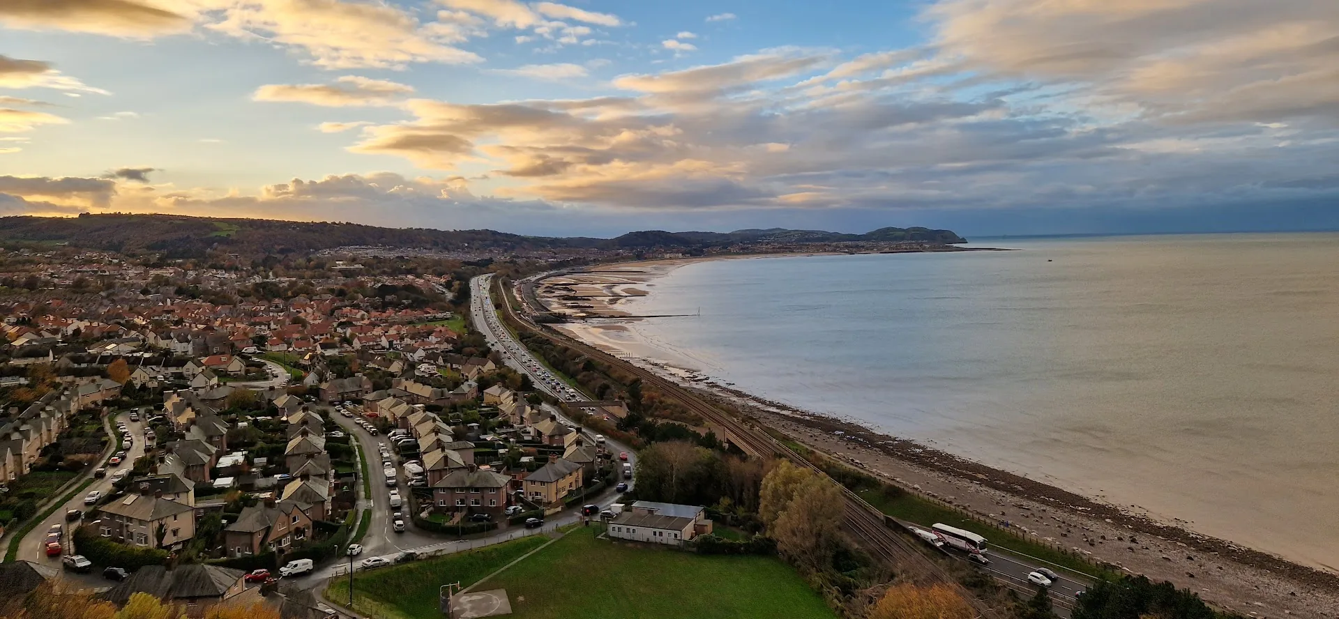 Colwyn Bay seen from Penmaenhead at dusk, the beach curving away west with the town spread up the slope behind it
