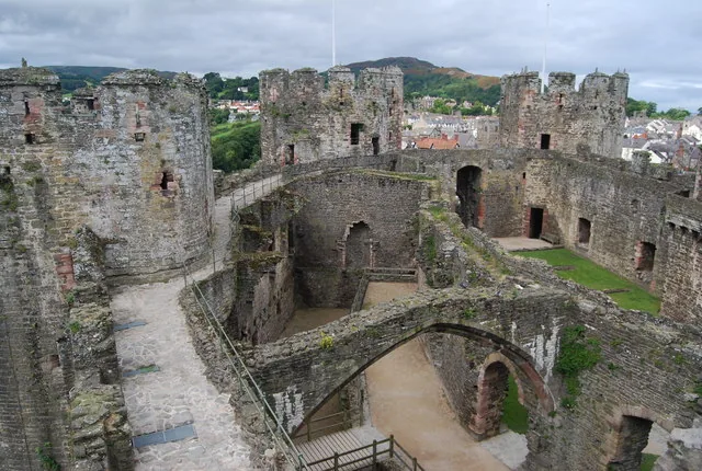 An elevated view inside Conwy Castle showing the roofless Great Hall, several towers, and the town and hills beyond the walls.
