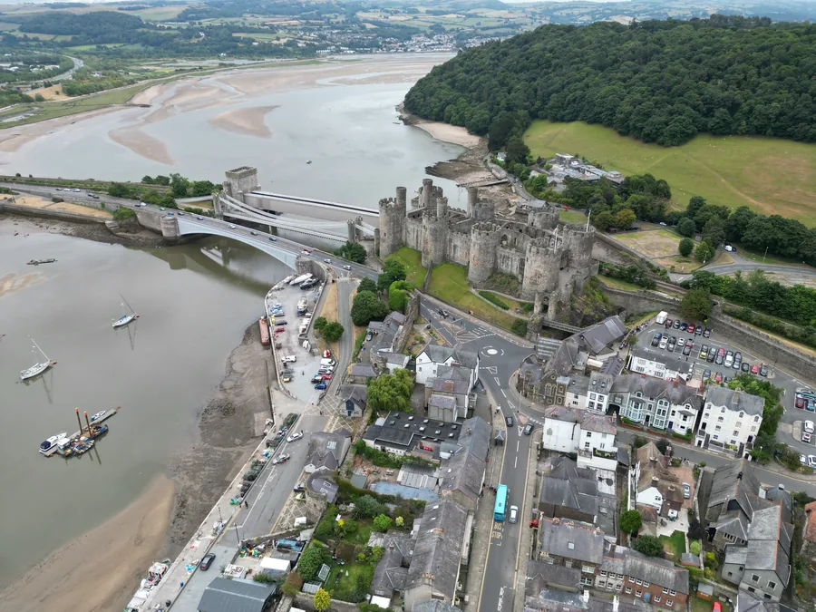 An aerial view of Conwy, its 13th-century castle and town walls above the estuary, the suspension bridge and railway bridge crossing the river beside it.