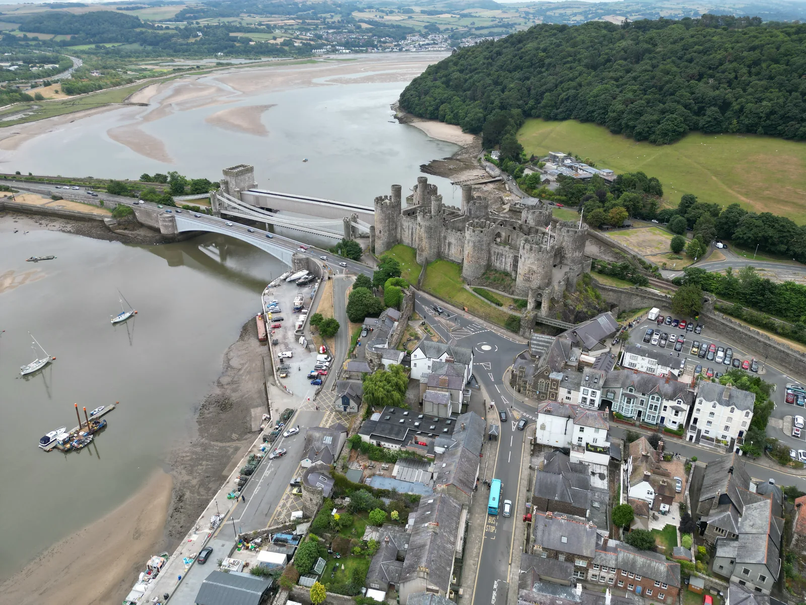 An aerial view of Conwy, its 13th-century castle and town walls above the estuary, the suspension bridge and railway bridge crossing the river beside it