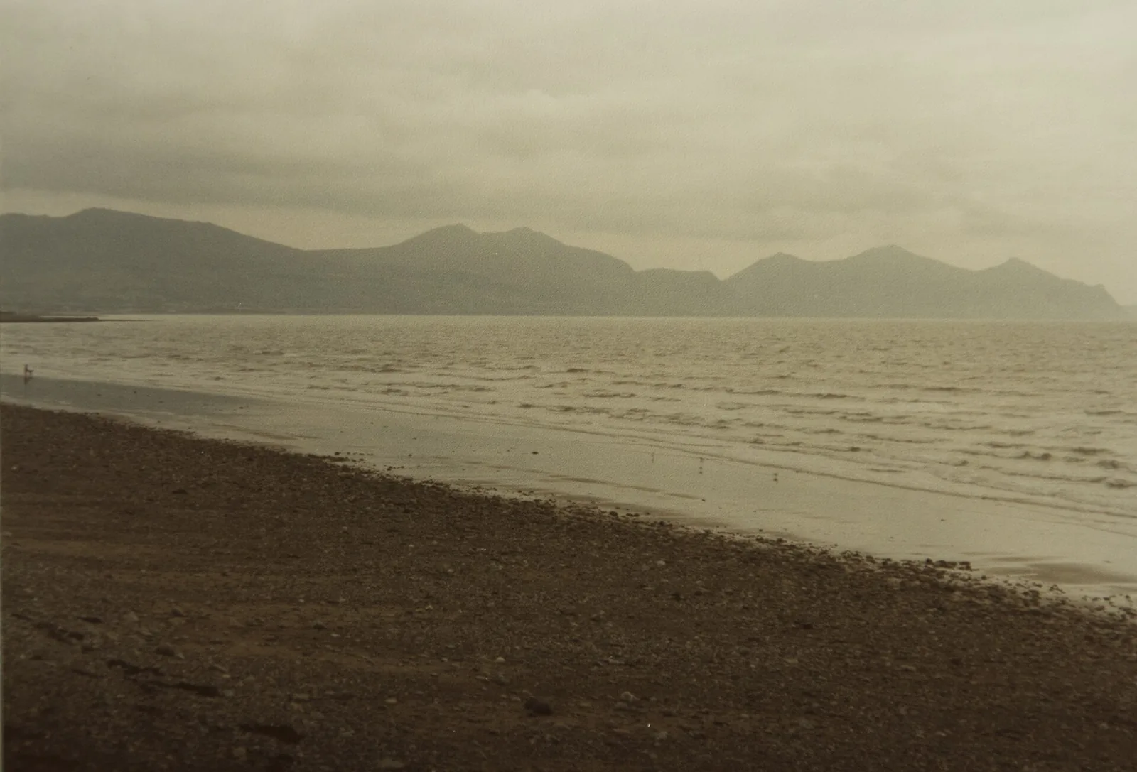 A wide, quiet beach at Dinas Dinlle with hazy mountains of the Llŷn Peninsula visible across the water.